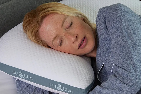 A woman sleeping resting her head on Eli & Elm side sleeper pillow with her hand tucked under the pillow