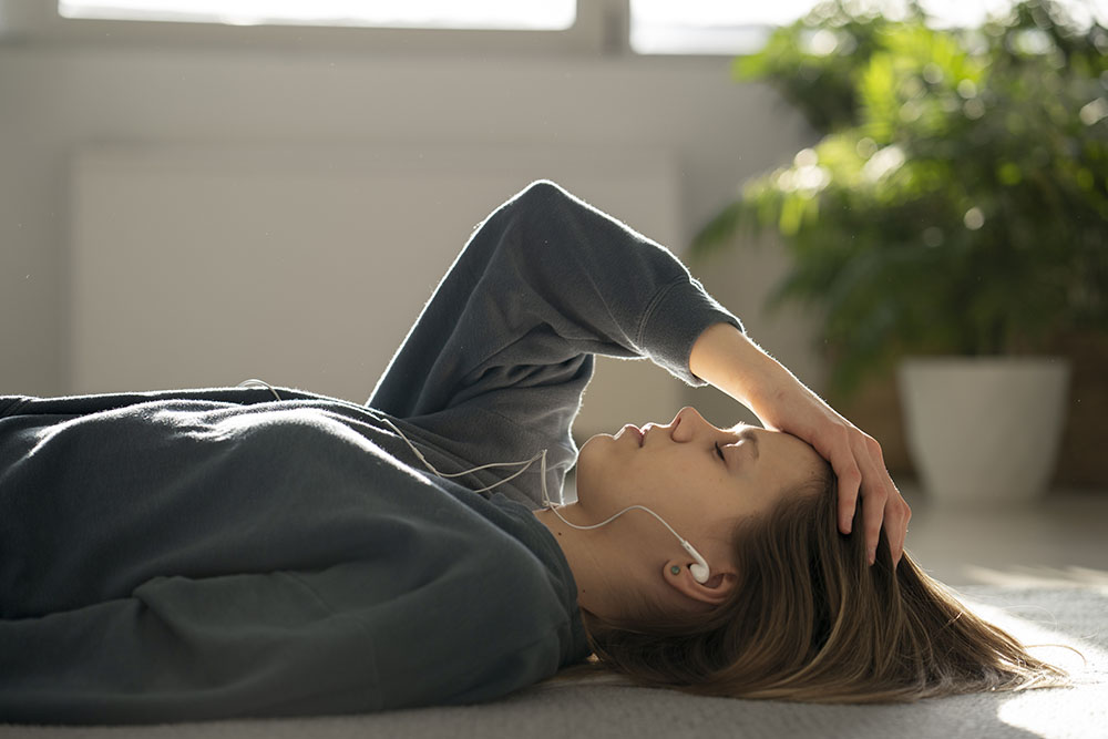 A woman lying down with her hand on her forehead, indicating a headache.
