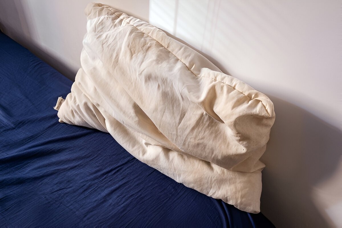 Old used white pillow with yellow stains placed on a blue bedding