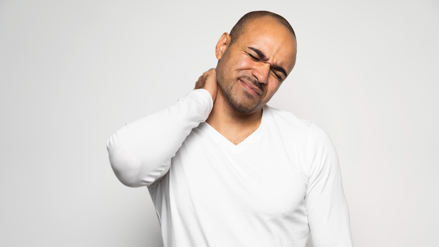 A man putting his arm on the back of his neck, suffering from neck pain.