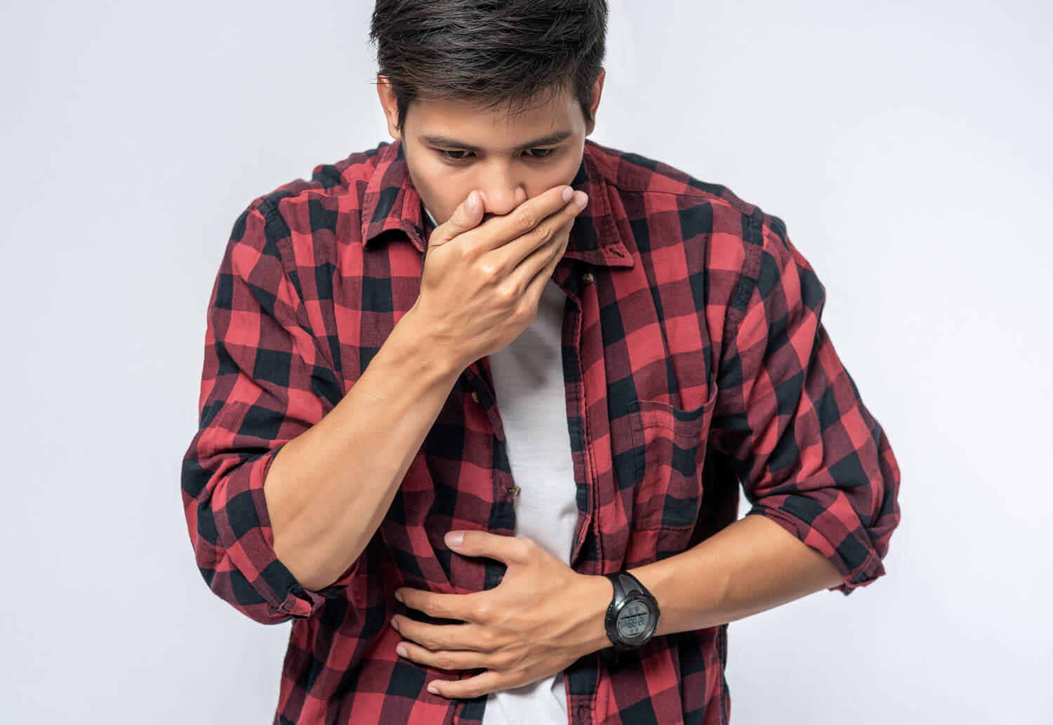 A man in a red and black check shirt puts his hands over his stomach and mouth, emphasizing on digestive issues