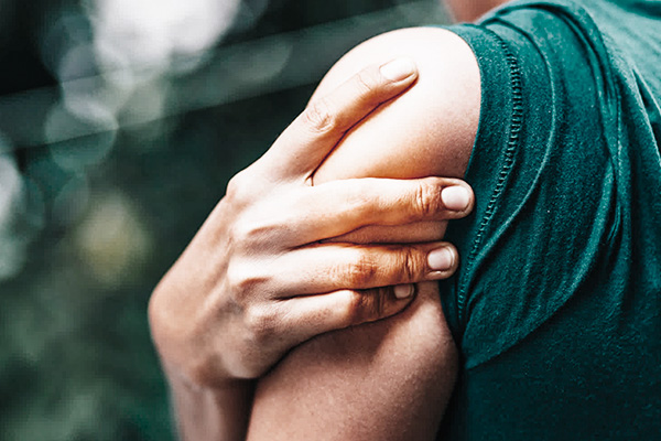 A person with his hand over his shoulder signals shoulder pain on a greenish background