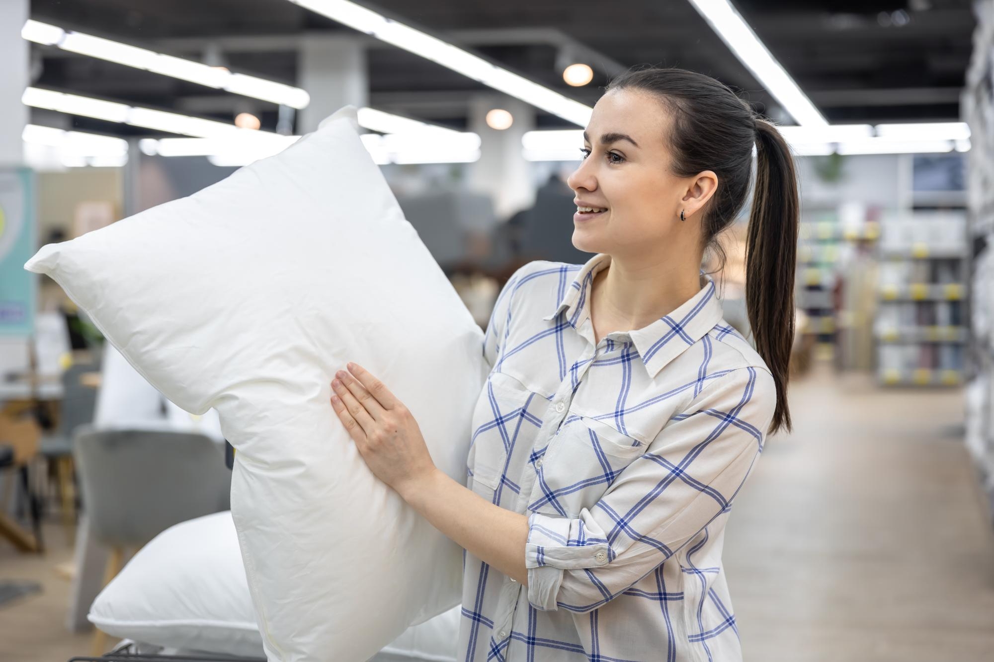 A woman holding a white pillow checking its quality and loft.