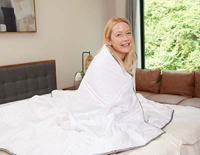 A woman sitting on a bed with Eli & Elm weighted comforter wrapped around her