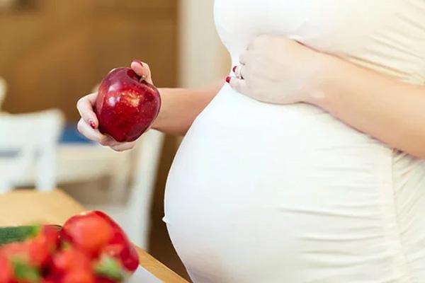 A pregnant woman holding an apple