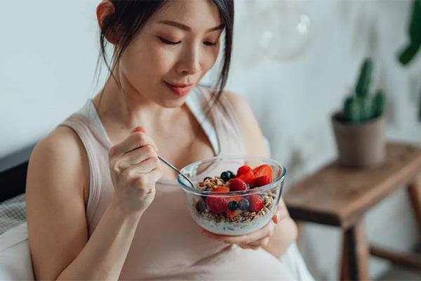 A pregnant woman eating a healthy diet of fruits and berries from a bowl