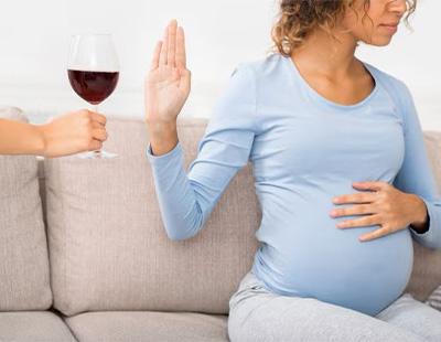 A pregnant gesturing her hand to refuse wine consumption during pregnancy.