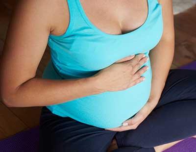A pregnant woman sits with her legs crossed and holds her belly