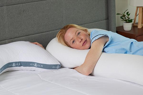 A woman lies on her side with arms wrapped around the Eli & Elm pregnancy pillow beside the side sleeper pillow