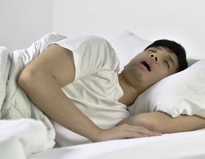 A man sleeping on his side with his mouth open and hand tucked under a pillow indicating sleep apnea