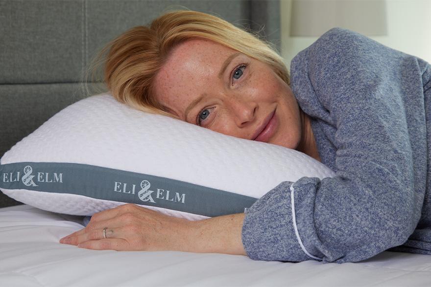 A woman resting her head on a white Eli & Elm cooling side sleeper pillow with her hand tucked under