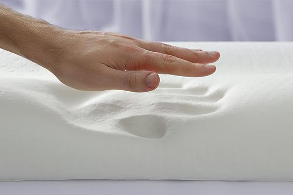 A hand exploring the surface of a white memory foam pillow which left an imprint upon pressing.