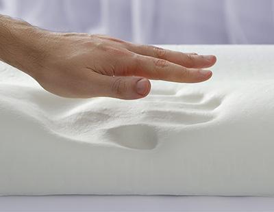 A hand explores the surface of a white memory foam pillow, which leaves an imprint upon pressing