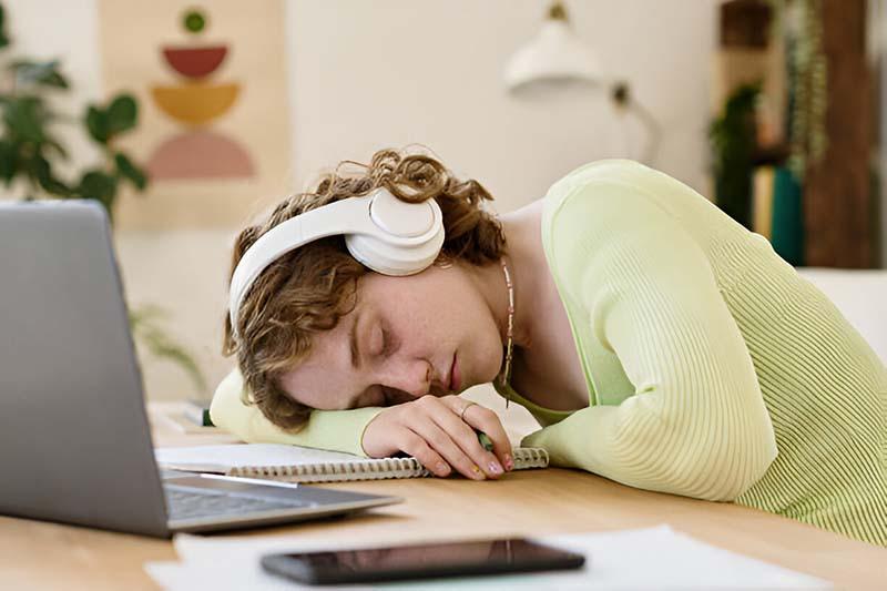 A young female student napping with her headphones on, keeping her head on the copybook