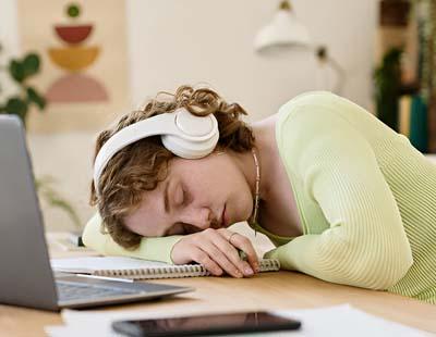 A young female student napping with her headphones on, keeping her head on the copybook