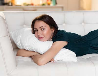 A woman sleeping on her stomach on a couch with a pillow wrapped around her arms