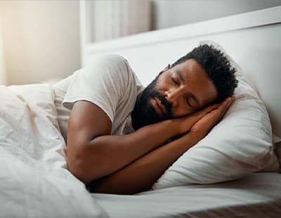 A man sleeping with both arms folded in a prayer position under his head.