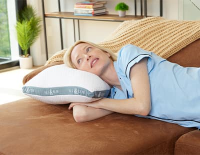 A woman lying on a couch resting her head on Eli & Elm's side sleeper cooling pillow