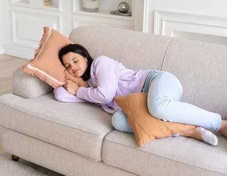 A women sleeping with a pillow between their legs on a couch.