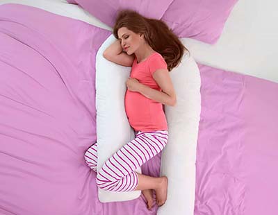 A pregnant woman sleeping on her side with a U-shaped body pillow