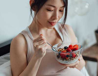 A pregnant woman eating a healthy diet of fruits and berries from a bowl