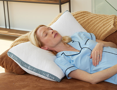 A woman lying on a brown couch, resting her head on the Eli & Elm Side sleeper pillow