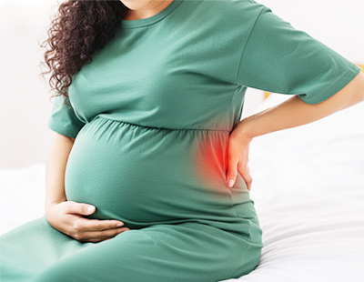 A pregnant woman sitting with her hand on her back, emphasizing the sciatica pain she is suffering