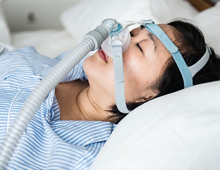 A woman using a CPAP device sleeping on a CPAP pillow.
