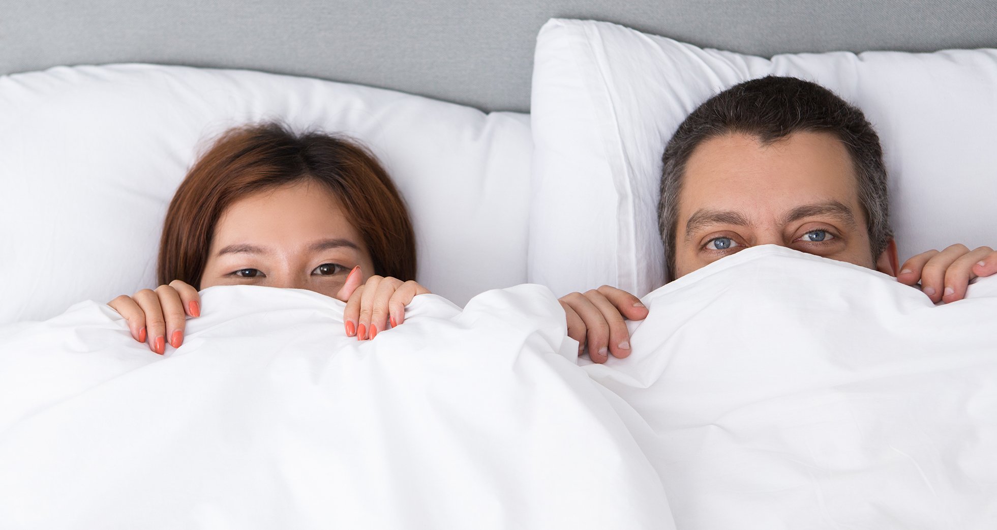 A woman and a man peeking through the comforter.