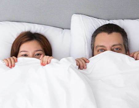 A woman and a man peeking through the comforter.