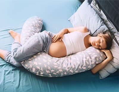 A pregnant woman sleeping on her side wrapped around a full-body pregnancy pillow