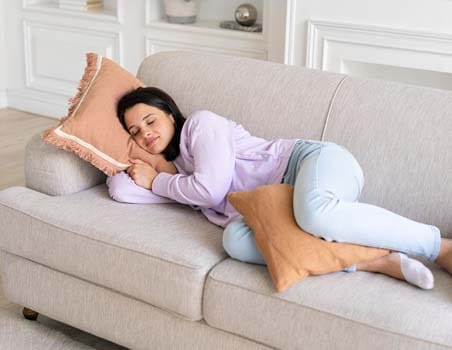 A women sleeping with a pillow between their legs on a couch.