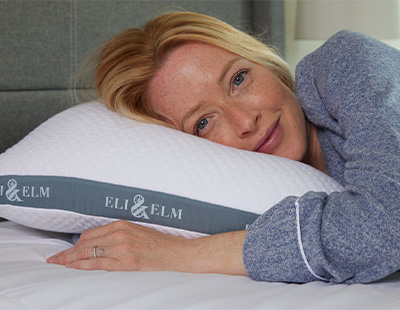 A woman resting her head on a white Eli & Elm cooling side sleeper pillow with her hand tucked under