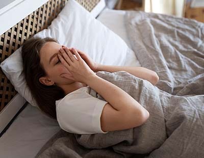 A woman in bed, unable to sleep, experiencing sleep deprivation