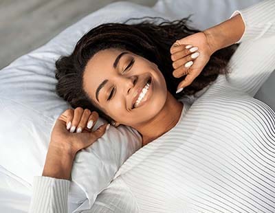 A woman waking up with a smile on her face, seemingly after experiencing a good night’s sleep