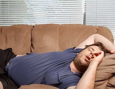 An overwieght man sleeping on the couch in a weird position and snoring