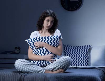 A woman sitting on her with a pillow, unable to sleep, emphasizing sleep deprivation