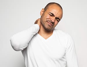 A man putting his arm on the back of his neck, suffering from neck pain.