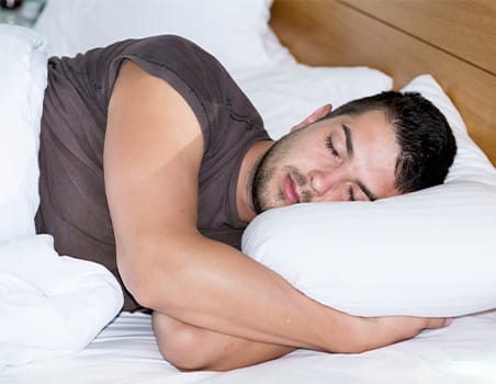 A man sleeping on his side with his hands folded underneath his head