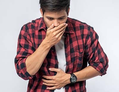 A man in a red and black check shirt puts his hands over his stomach and mouth, emphasizing on digestive issues