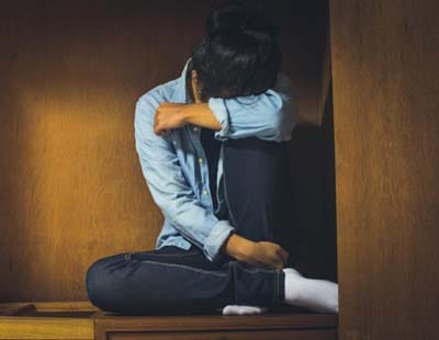 A young woman seated on a wooden bench in a room, symbolizing the struggles of women with post-traumatic stress disorder