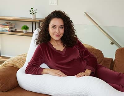 A pregnant woman sitting supported by a body pillow