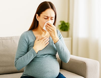 A pregnant woman suffering from allergies and sneezing into a napkin