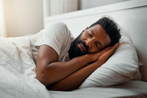 A man sleeping with both arms folded in a prayer position under his head.