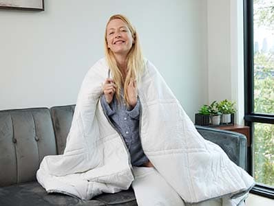 Woman sitting on the couch with a weighted comforter wrapped around her