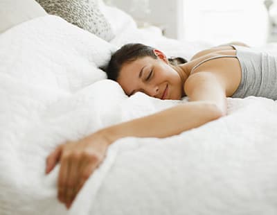A woman peacefully sleeping on her stomach in bed with her eyes closed.