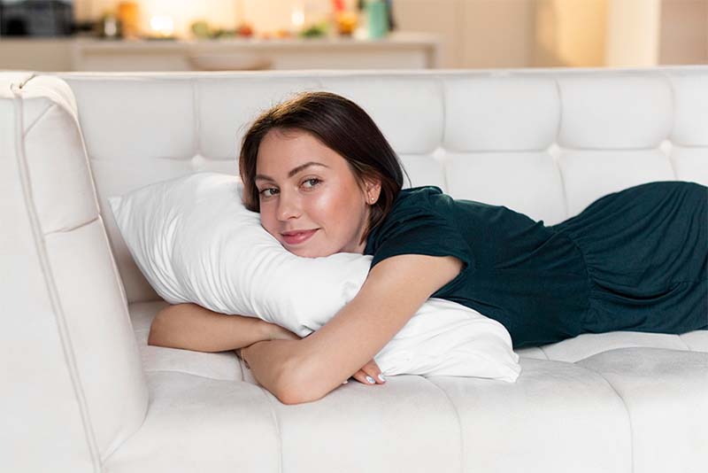 A woman sleeping on her stomach on a couch with a pillow wrapped around her arms