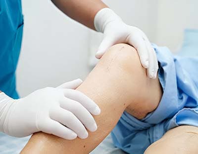 A healthcare professional in blue scrubs checks a patients knee