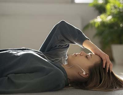 A woman lying down with her hand on her forehead indicating headache