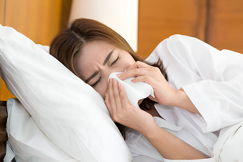 Woman sneezing in tissue on a bed and having difficulty sleeping because of a stuffy nose